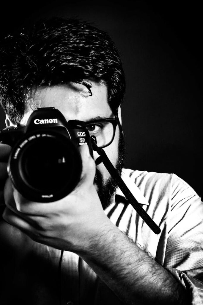 Black and white photo of a male photographer focusing his DSLR camera in a studio setting.